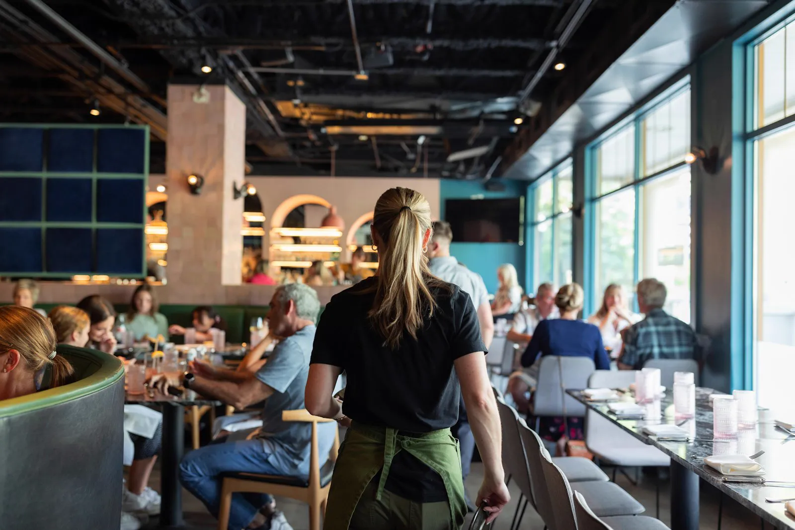 Server moving through a busy modern dining room mid-shift